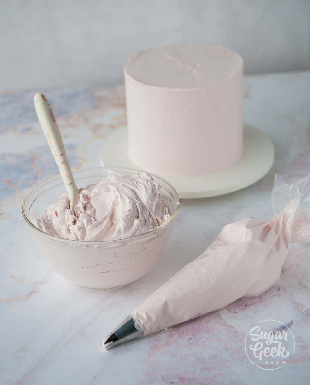 italian meringue buttercream in a bowl, piping bag and frosted no a cake