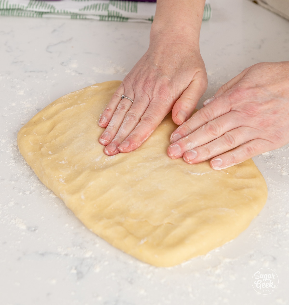 hands pressing down dough on a table
