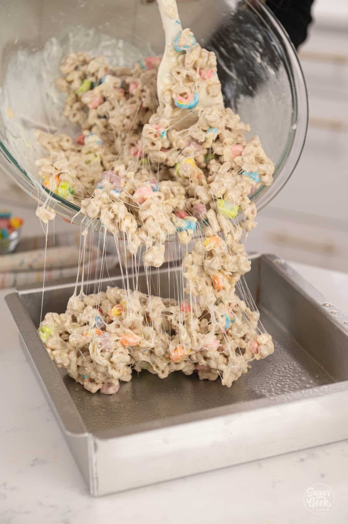 a bowl of cereal treat mixture pouring into a baking dish