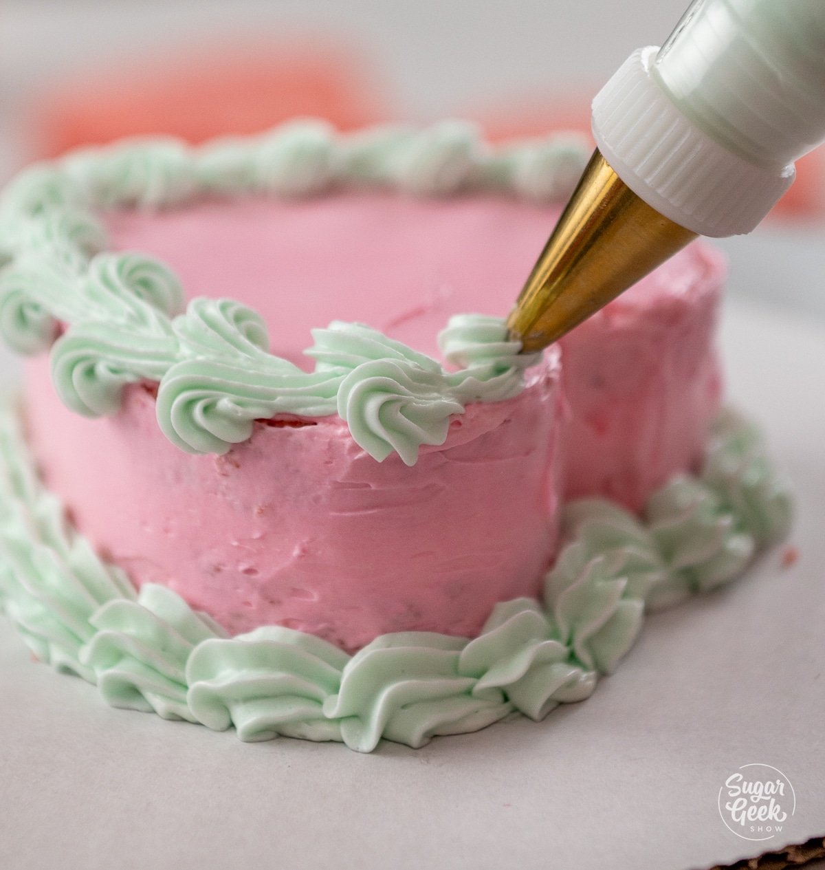 hand piping a green border with a piping bag on a pink heart cake
