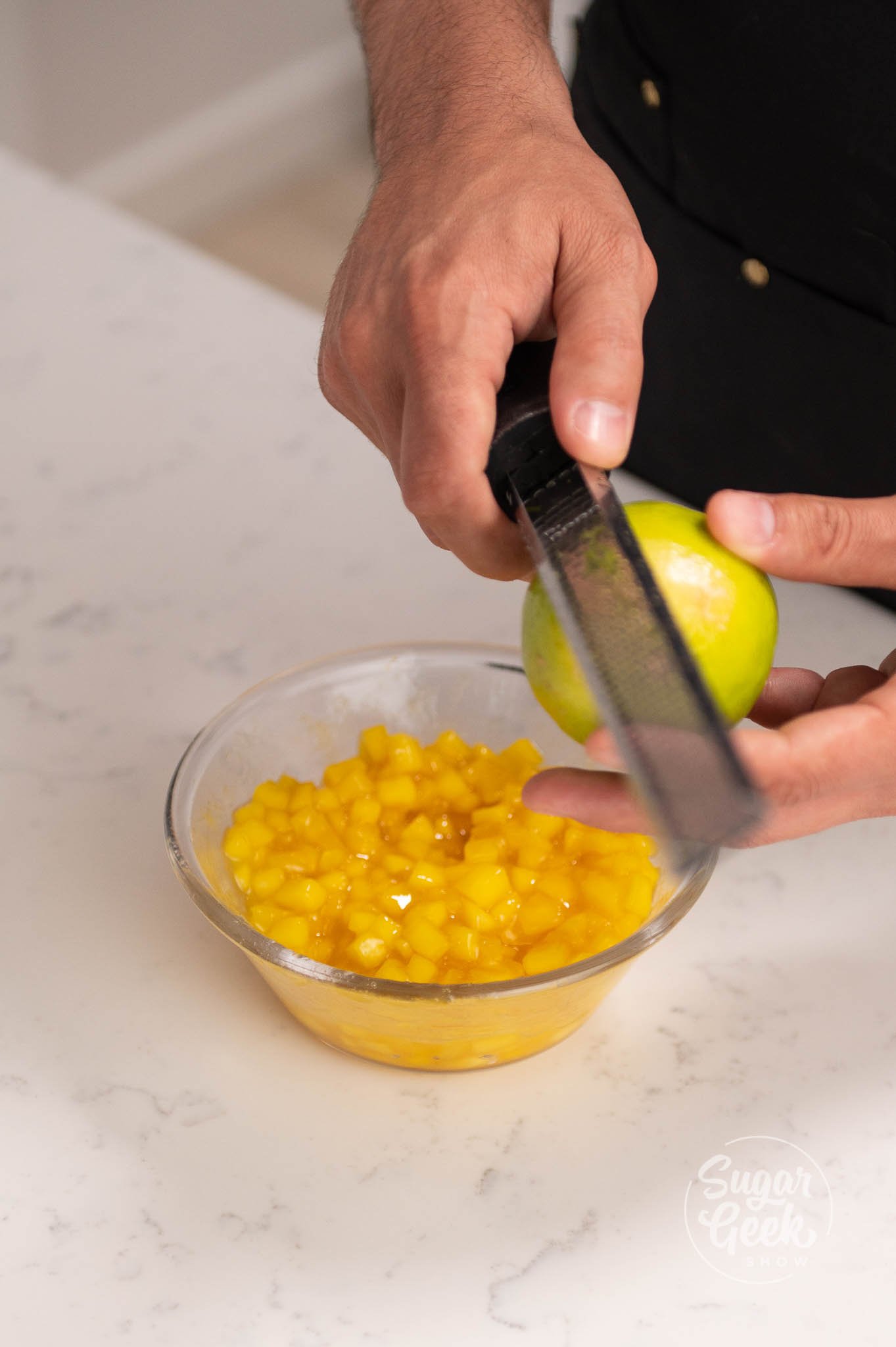 hands zesting a lime into bowl of compote