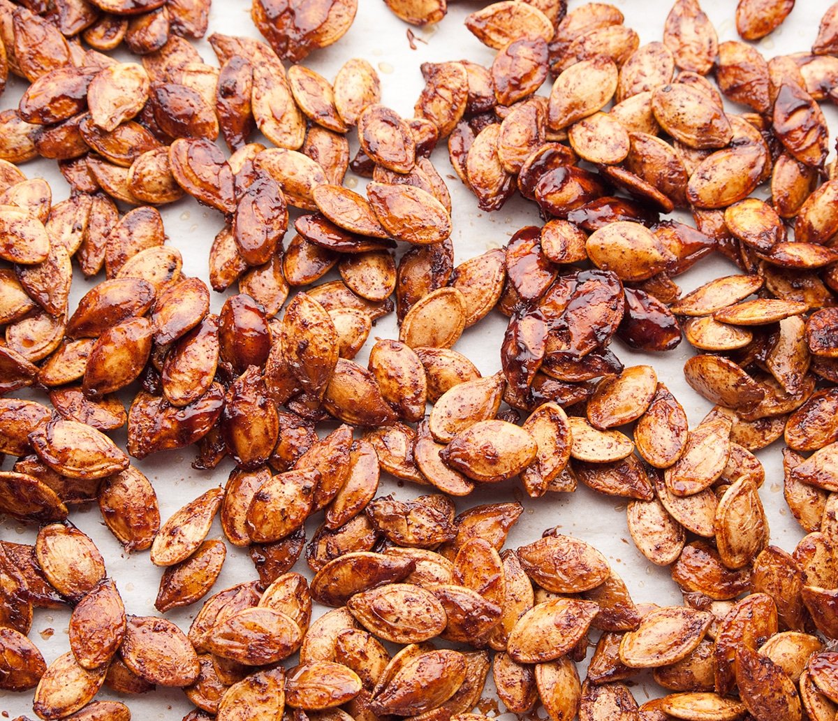 A parchment lined baking sheet is covered with roasted pumpkin seeds that were coated in maple syrup and spices- a delicious way to use up the leftover seeds from pumpkin carving. High point of view- looking down.