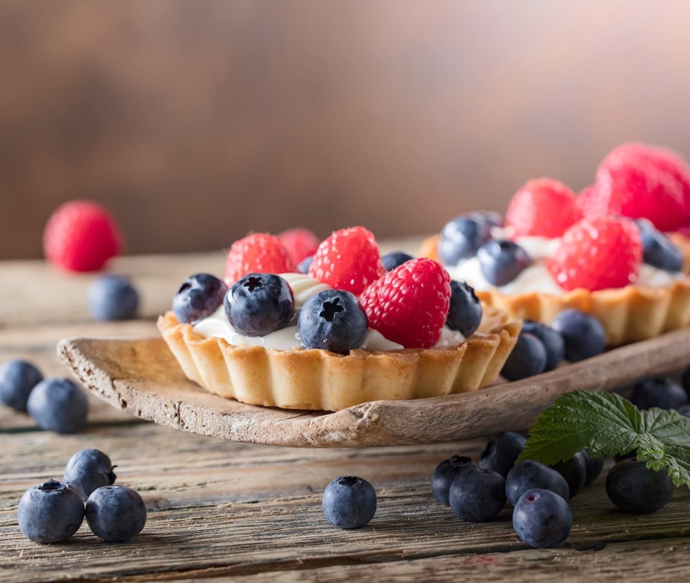Dessert tarts with raspberries and blueberries on a wooden table. Closeup of fancy gourmet fresh berry dessert tarts.