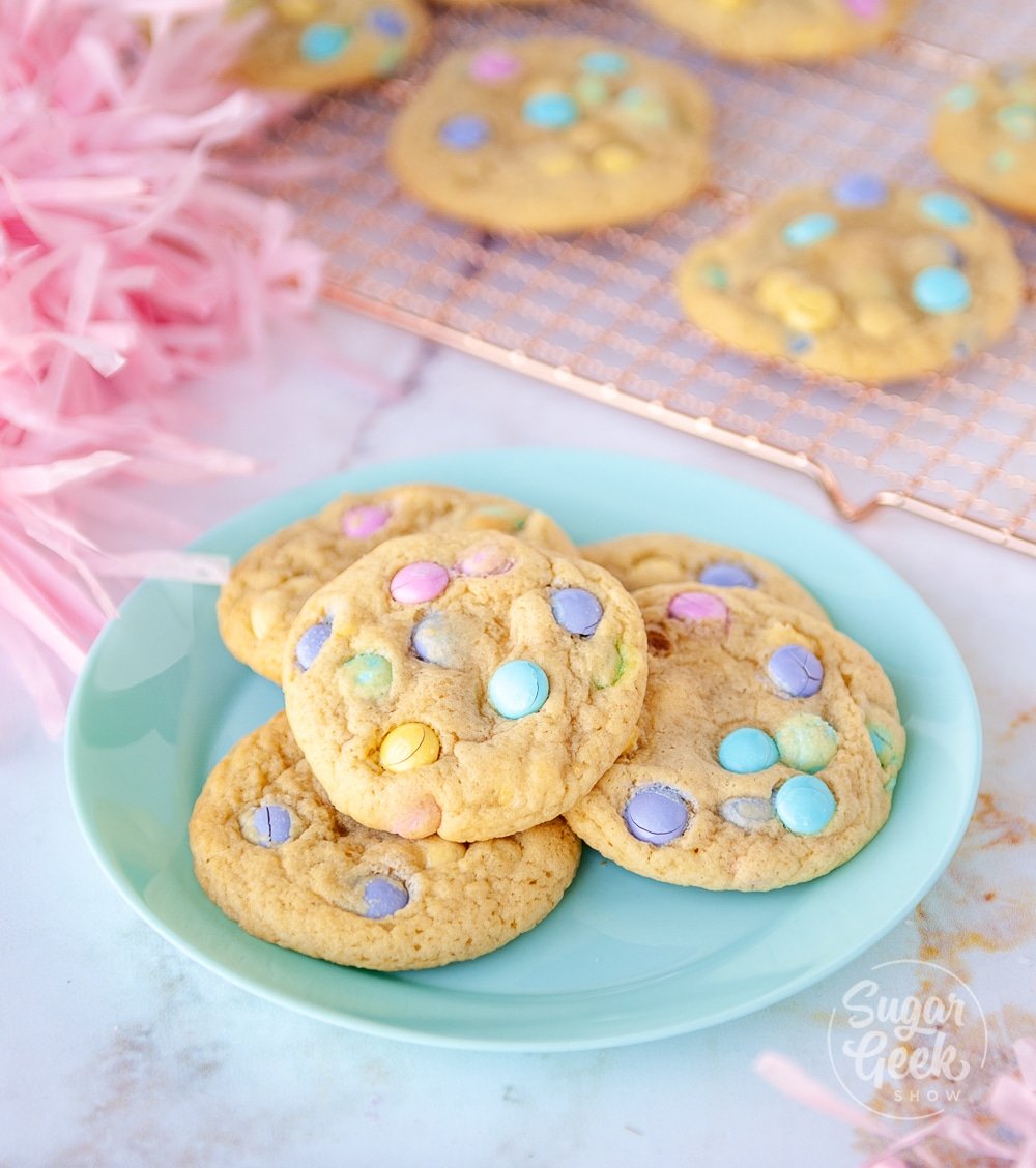 M&M cookies on a blue plate with more cookies on a cooling rack behind the plate