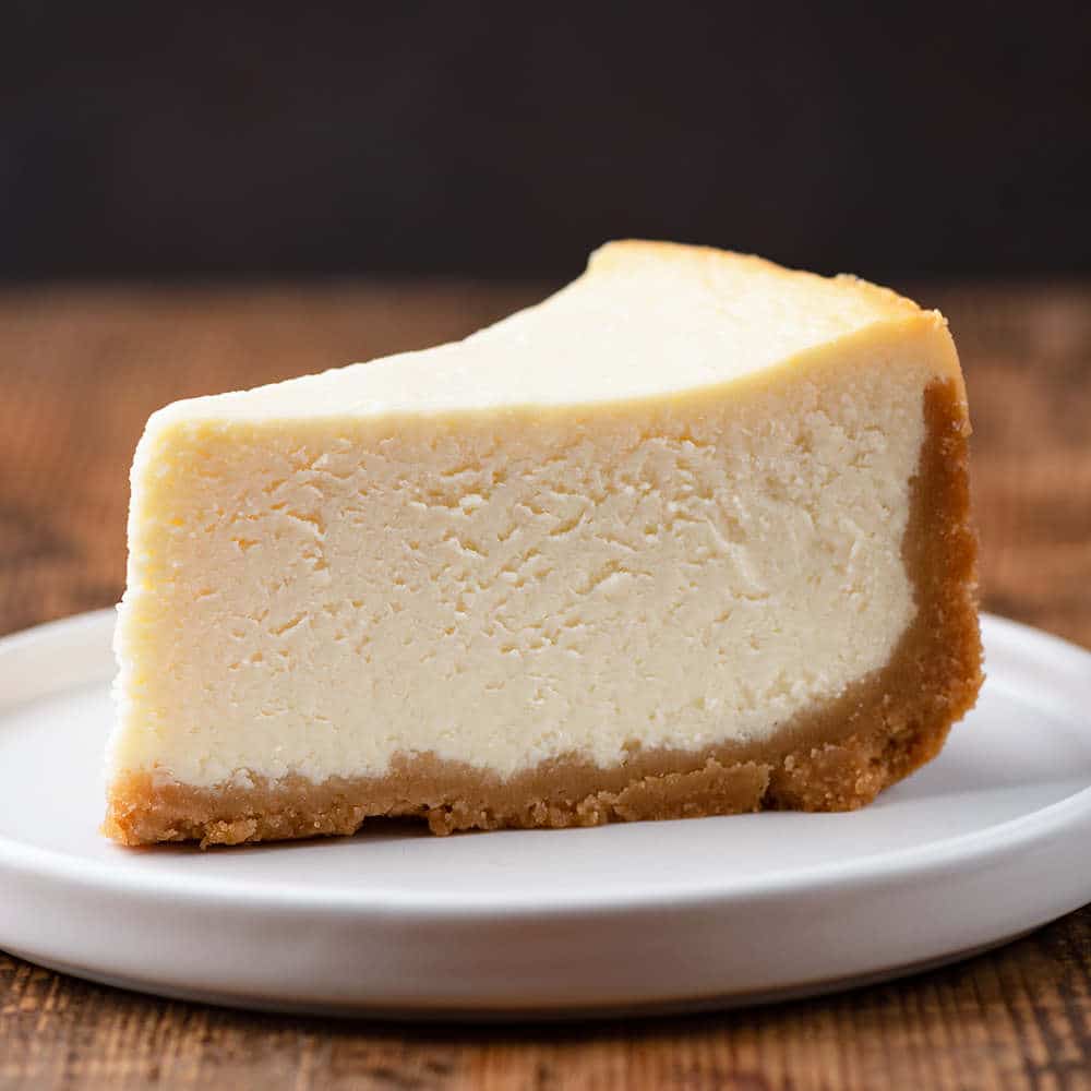 slice of New York cheesecake on a white plate with wooden background