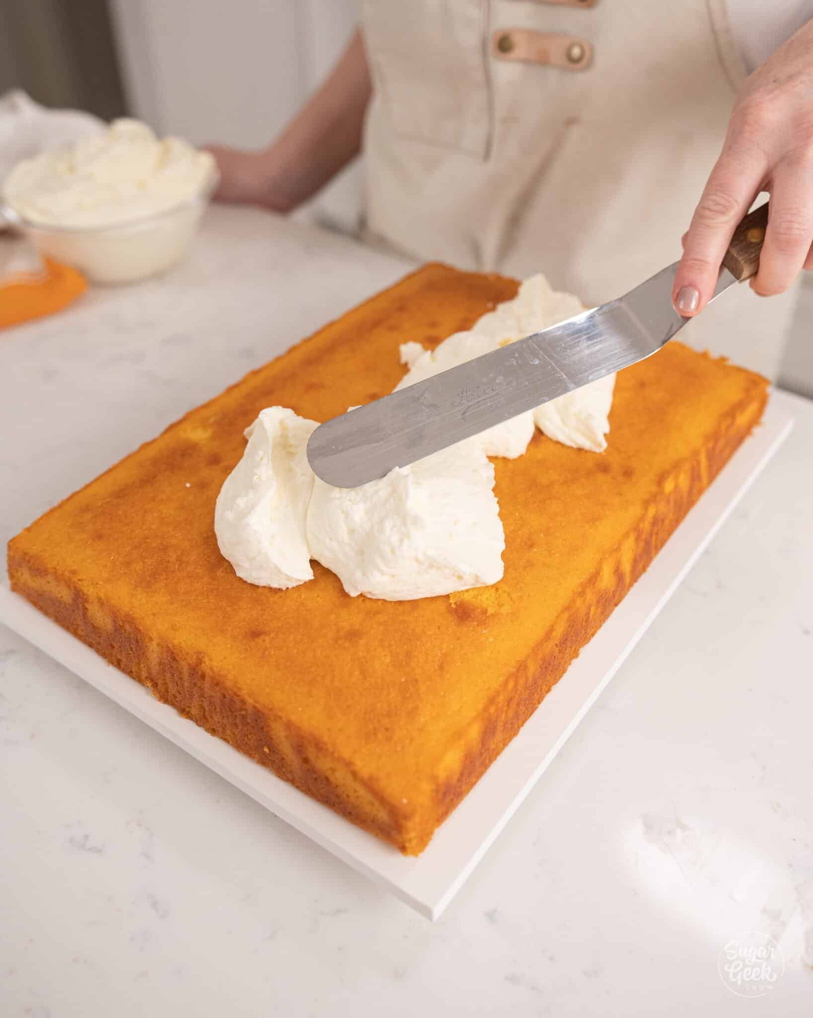 covering a rectangle orange cake with white frosting
