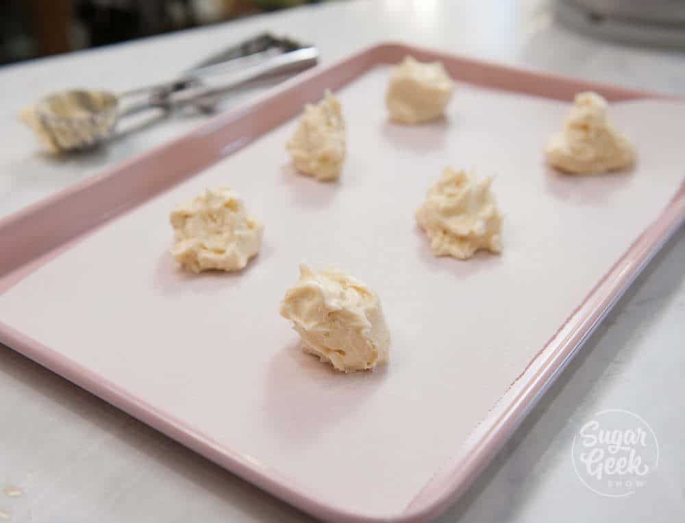 lofthouse cookie dough being portioned out onto a parchment lined cookie sheet with cookie scoop in the background