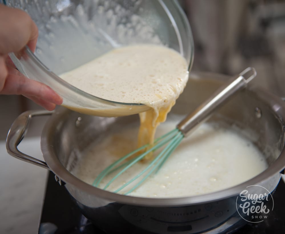 adding tempered egg mixture to stainless steel pan with blue whisk