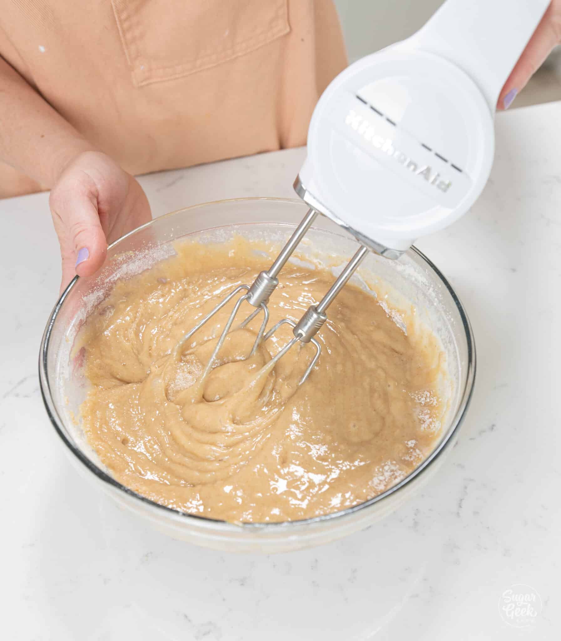 hands using hand mixer to mix together batter in bowl.