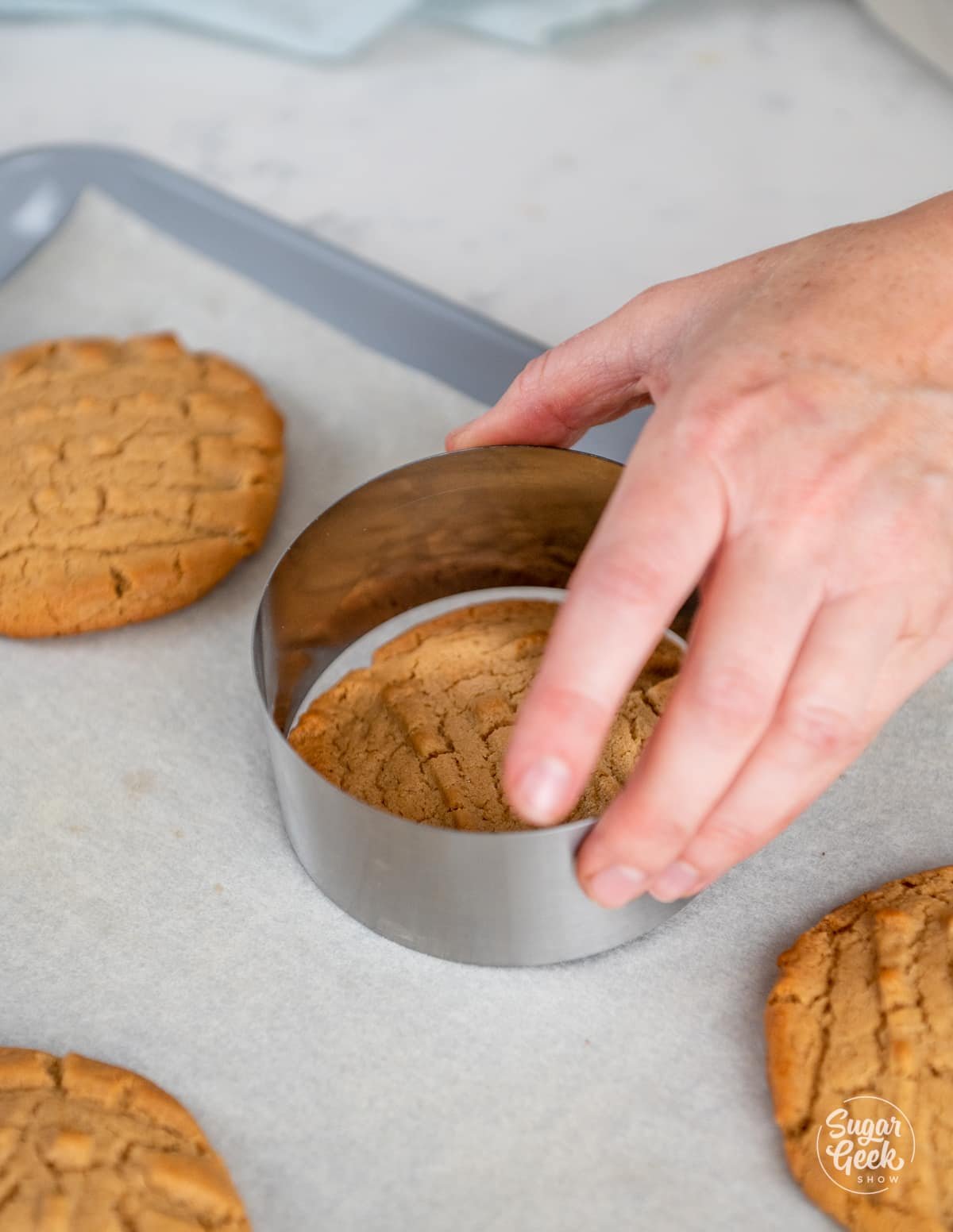 hand holding a metal circle cookie cutter on top of a peanut butter cookie