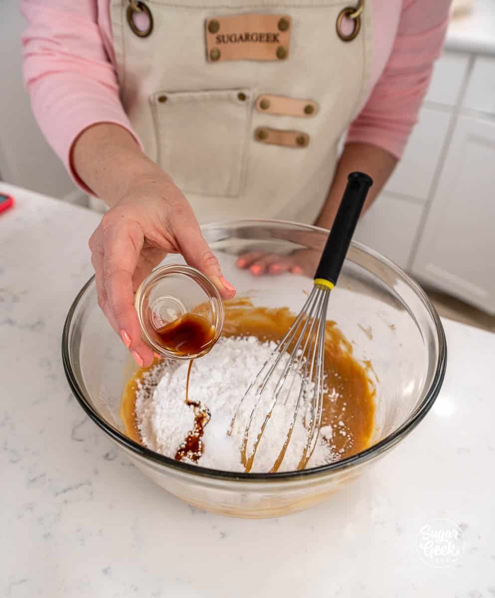 Hand adding a bowl of vanilla to apeanut butter mixture