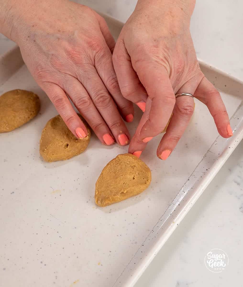 Hands laying a peanut butter egg on a sheet pan lined with parchment