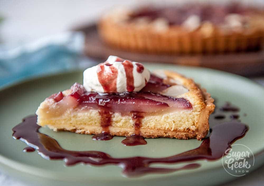 closeup slice of wine poached frangipane tart with whipped cream and drizzle of red wine sauce