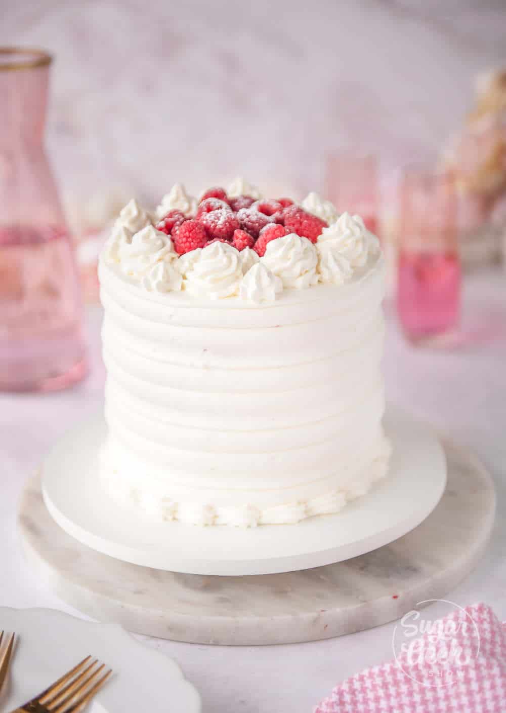 pink velvet cake frosted in stabilized whipped cream with fresh raspberries on top