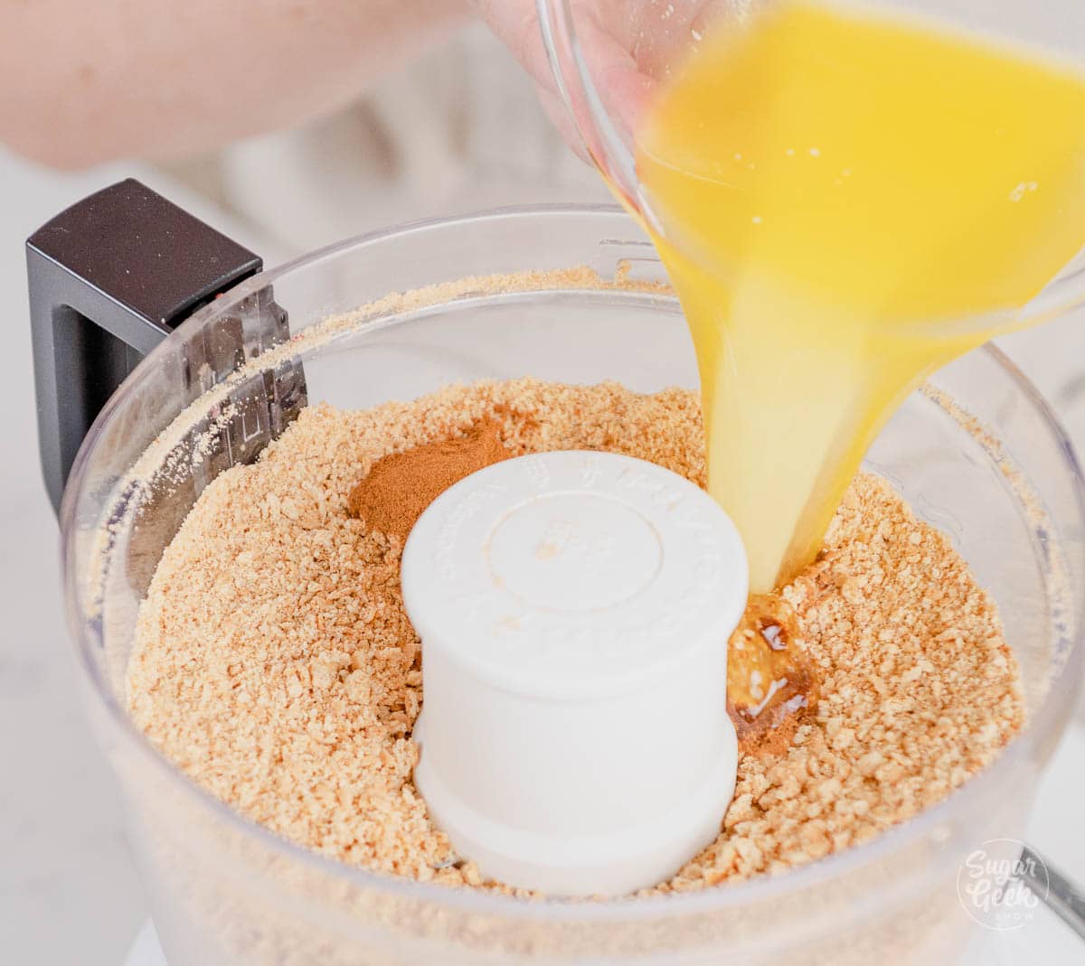 bowl of melted butter pouring into a food processor with graham crackers