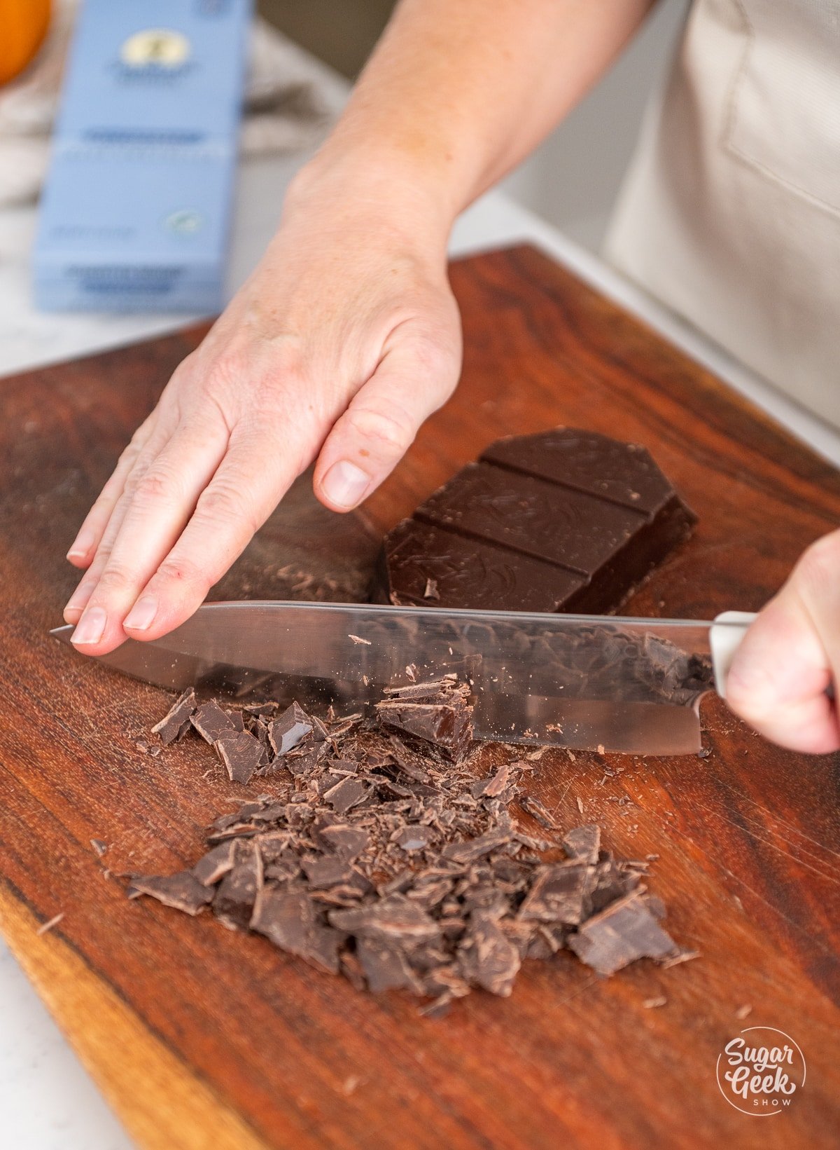 hands holding a chefs knife cutting a bar of chocolate on a cutting board