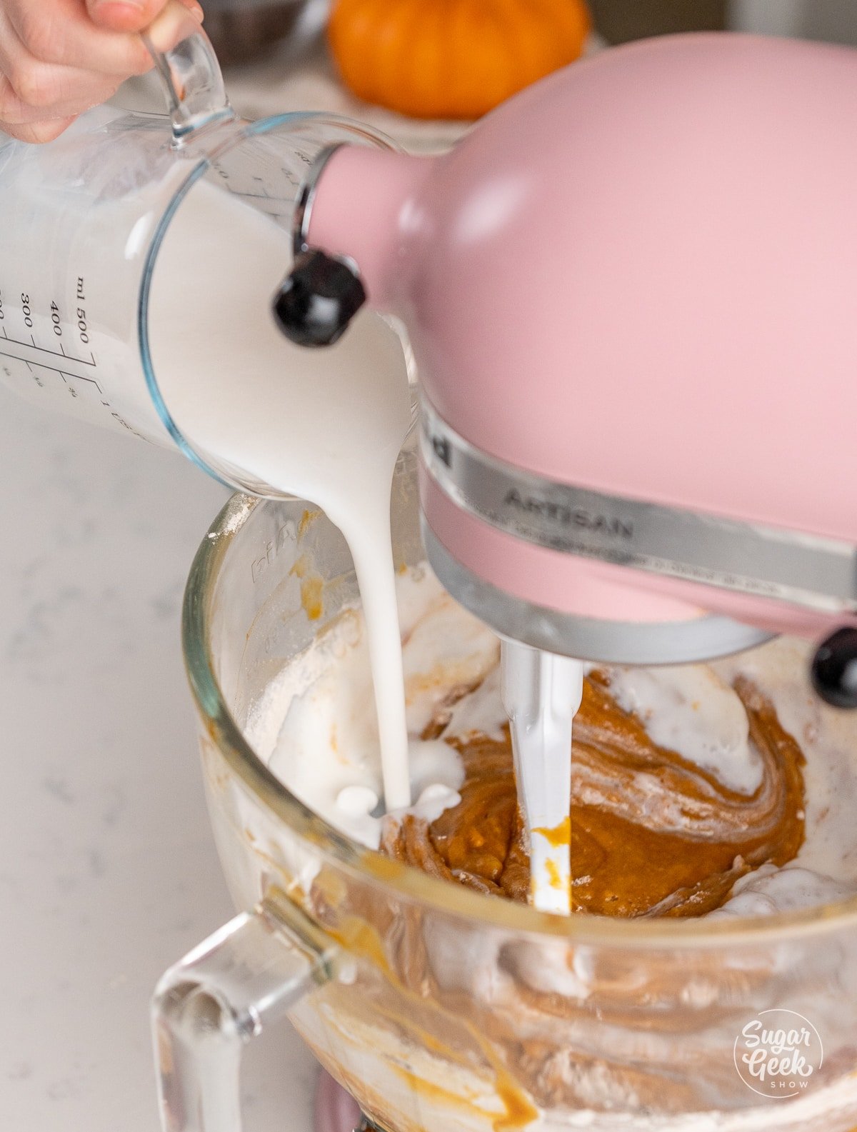 buttermilk pouring into a stand mixer bowl of pumpkin mixture