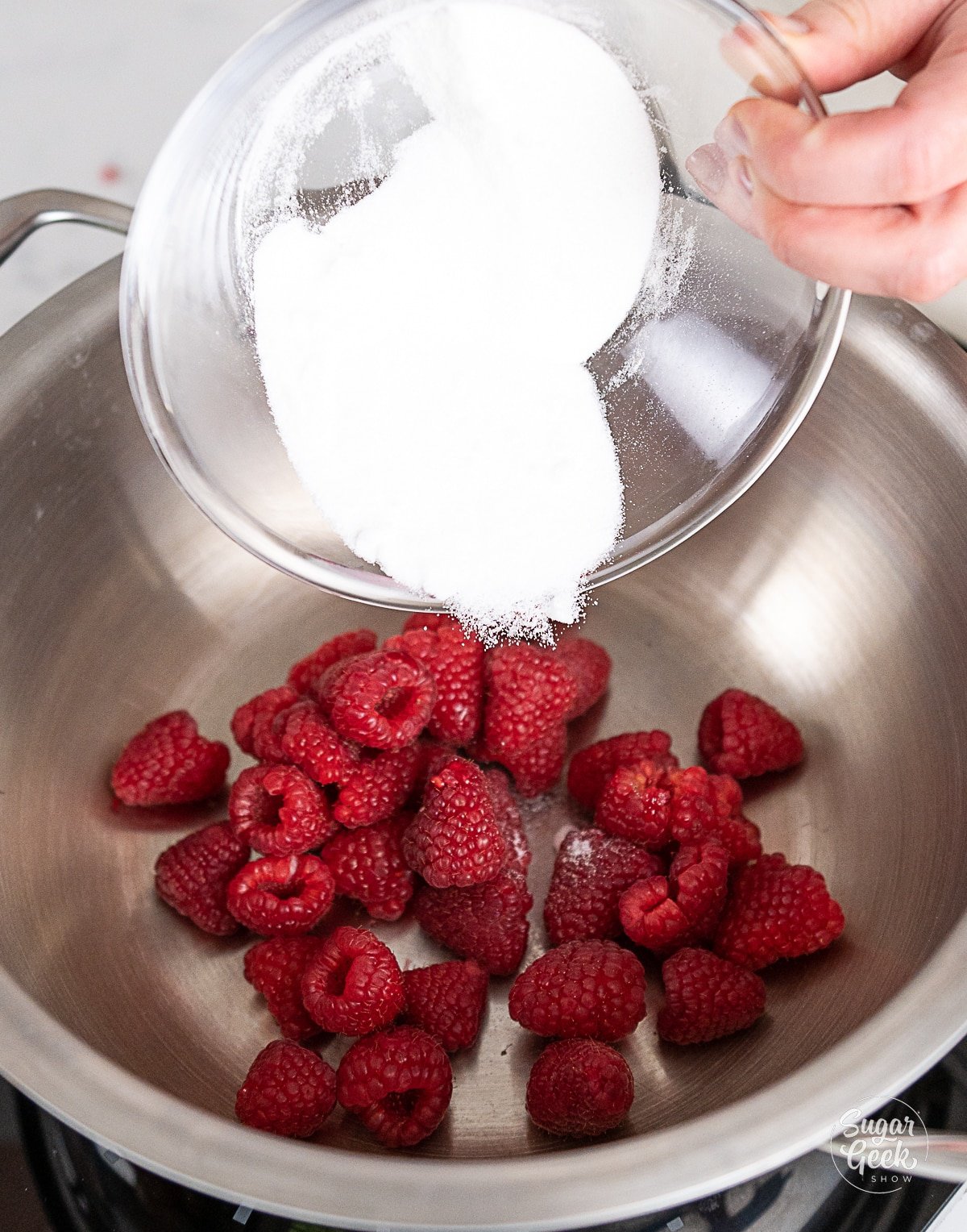 hand pouring sugar onto raspberries in a pot.