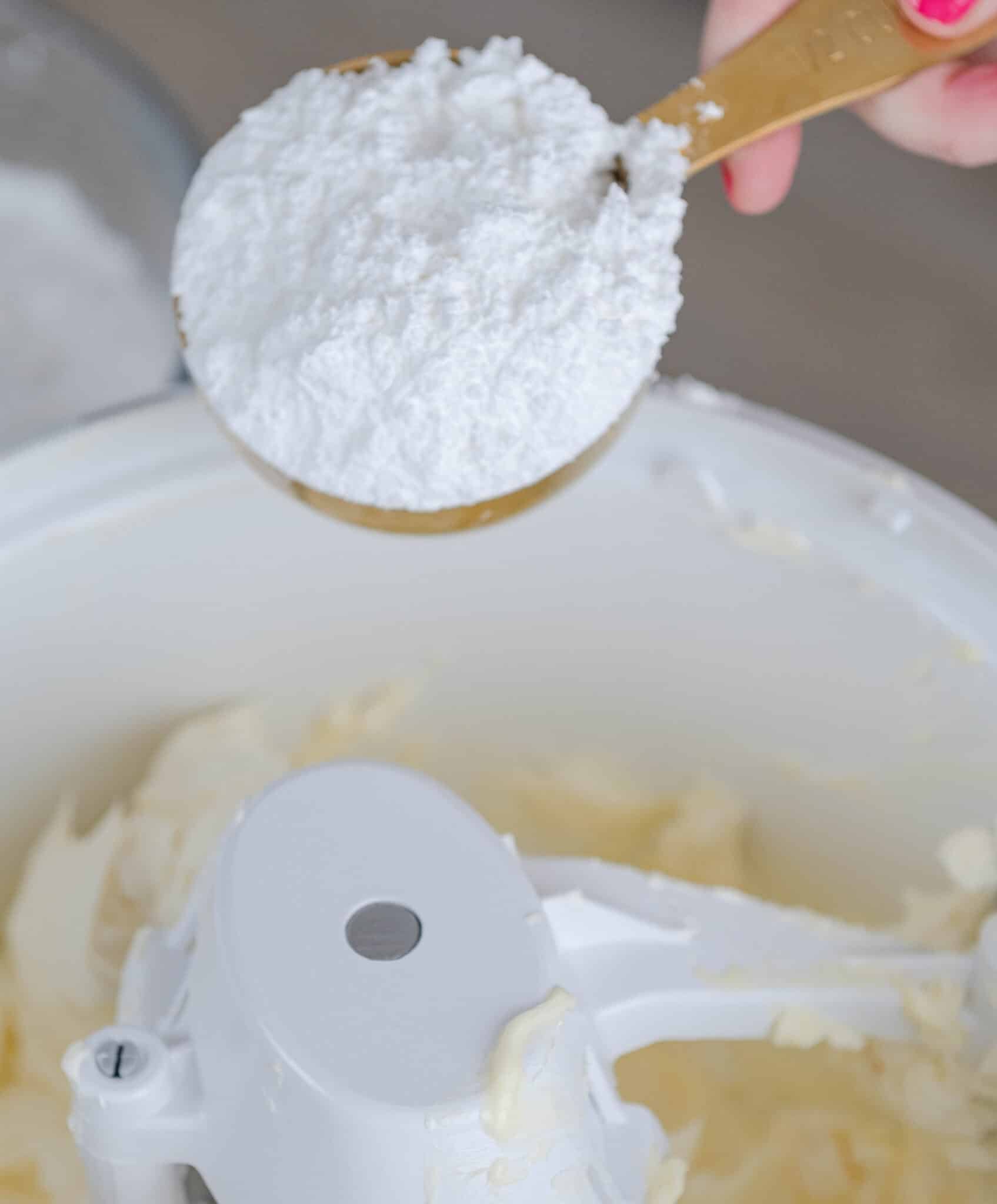 hand adding a cup of powdered sugar into a stand mixer bowl