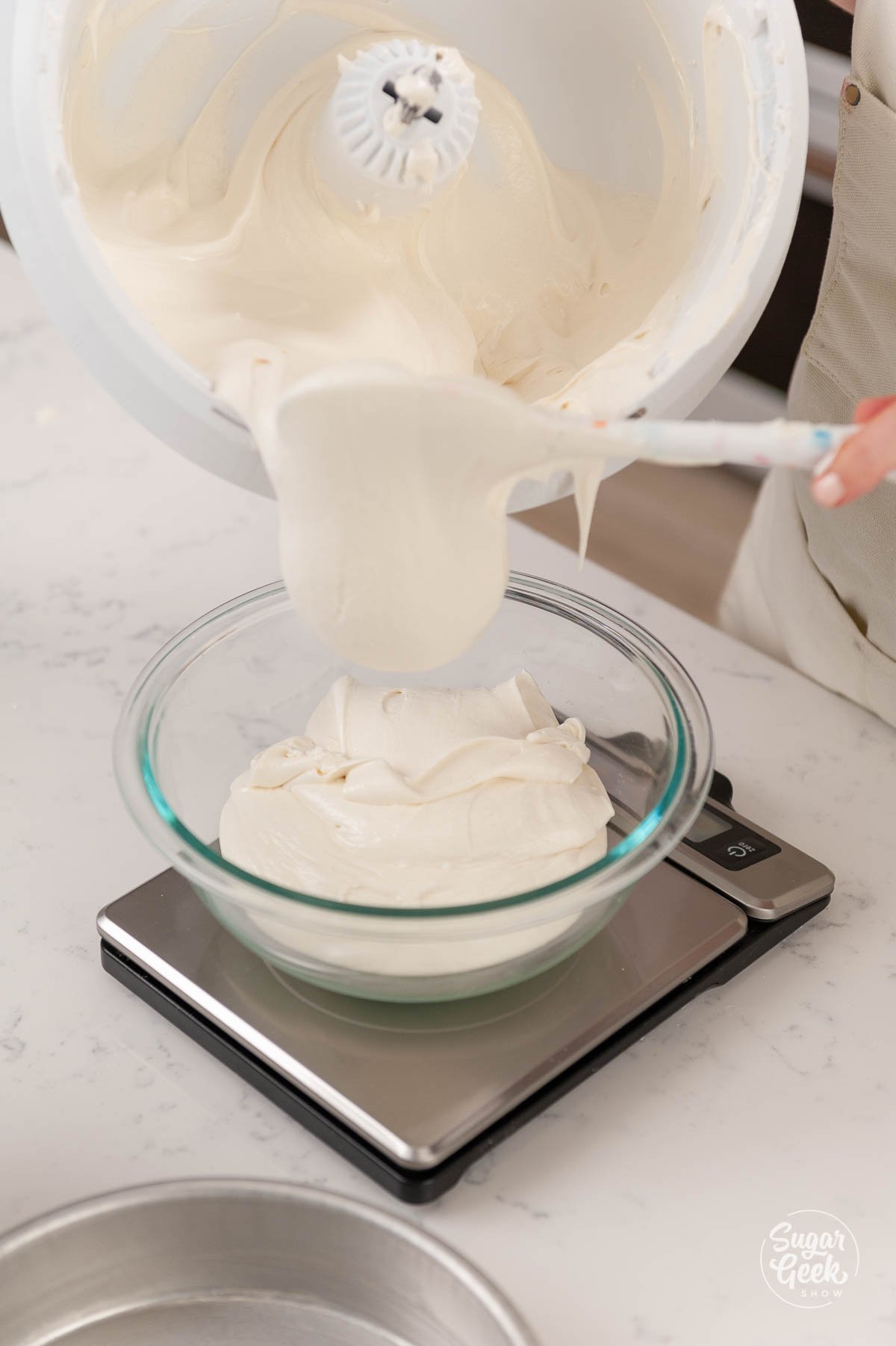 adding cake batter to a clear bowl on a kitchen scale