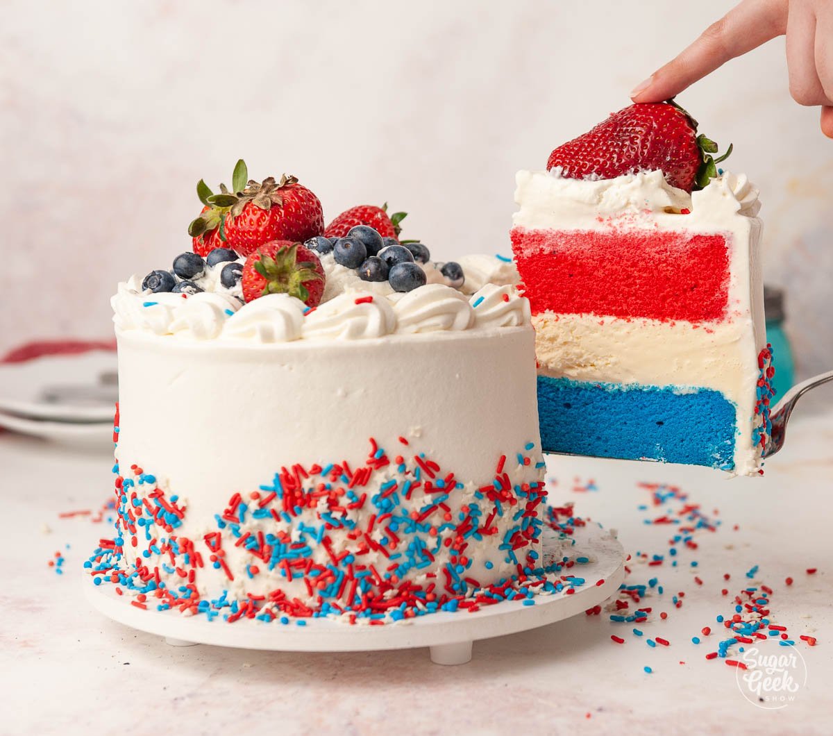 hand pulling a slice of red white and blue ice cream cake out of the main cake