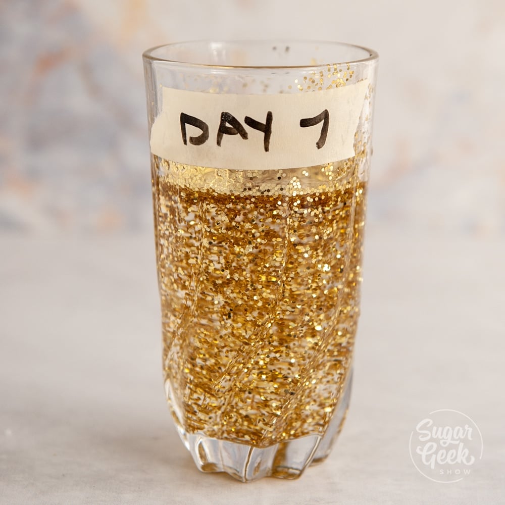 clear glass with water and lots of glitter inside. Tape on side that says "day 7" 
