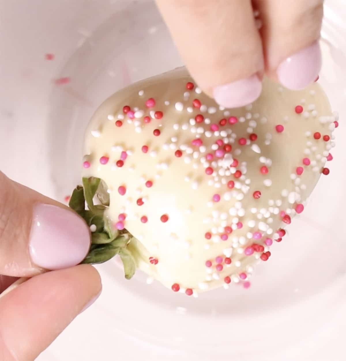 hands adding sprinkles to white chocolate covered strawberries shot from above
