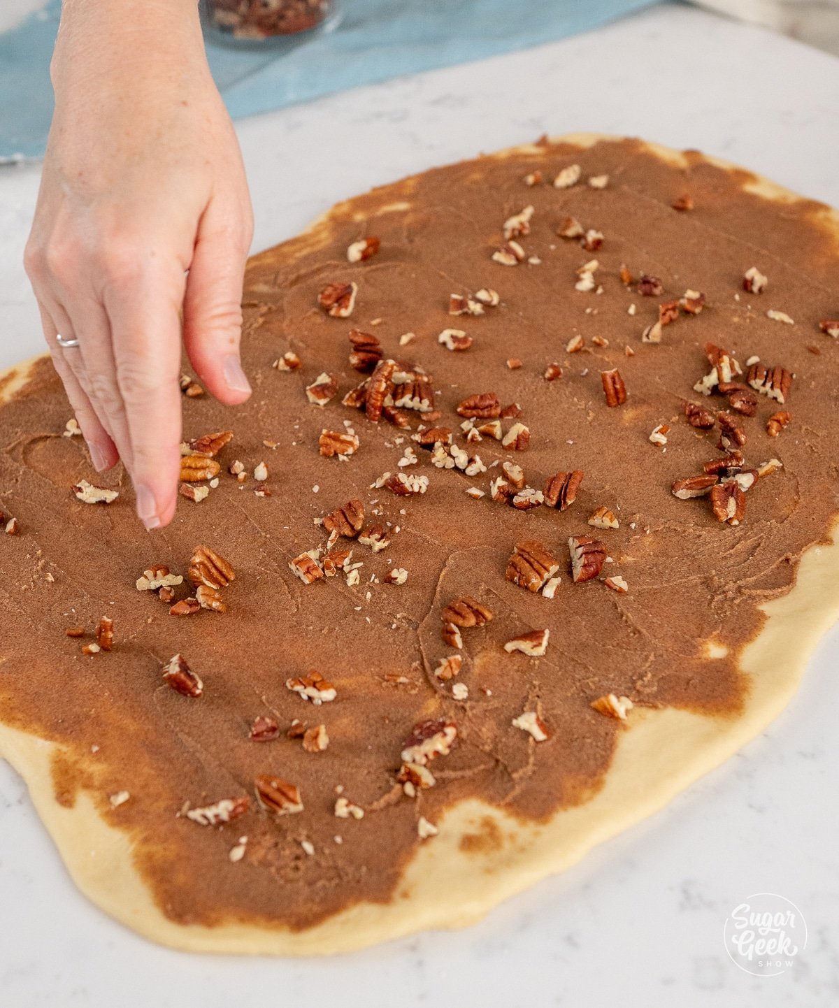 hand sprinkling pecans on top of a rectangle of dough