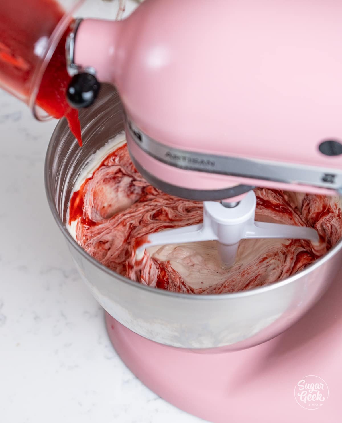 strawberry puree being added to a bowl of vanilla buttercream in a stand mixer