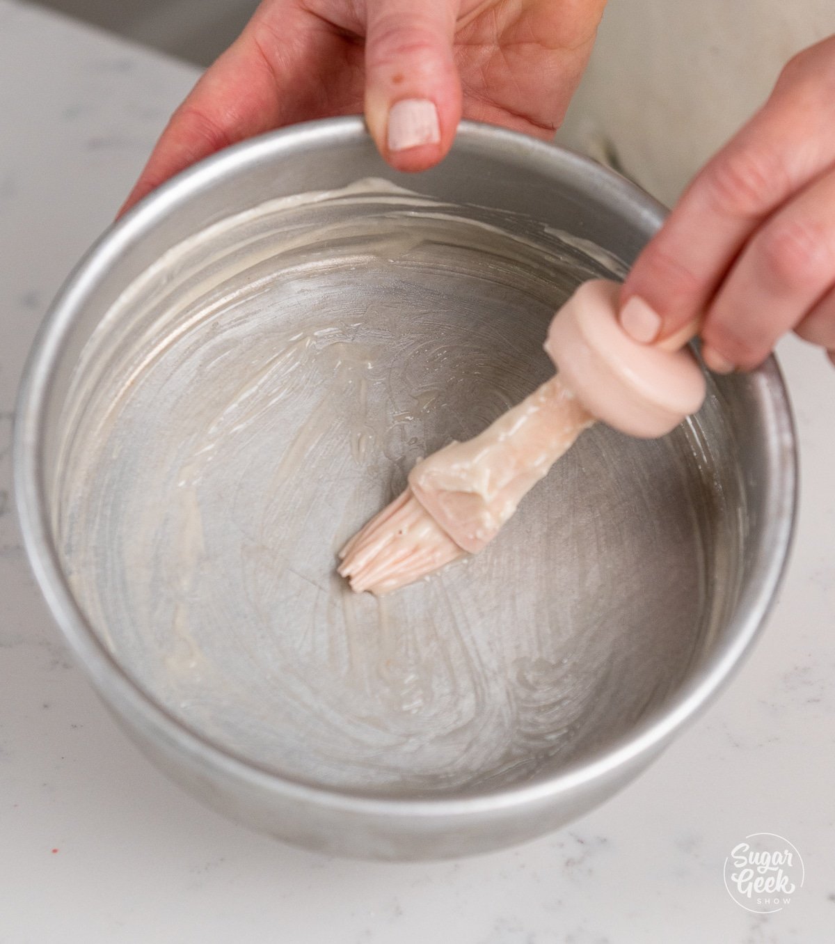 hands brushing cake goop into a cake pan with a pastry brush.