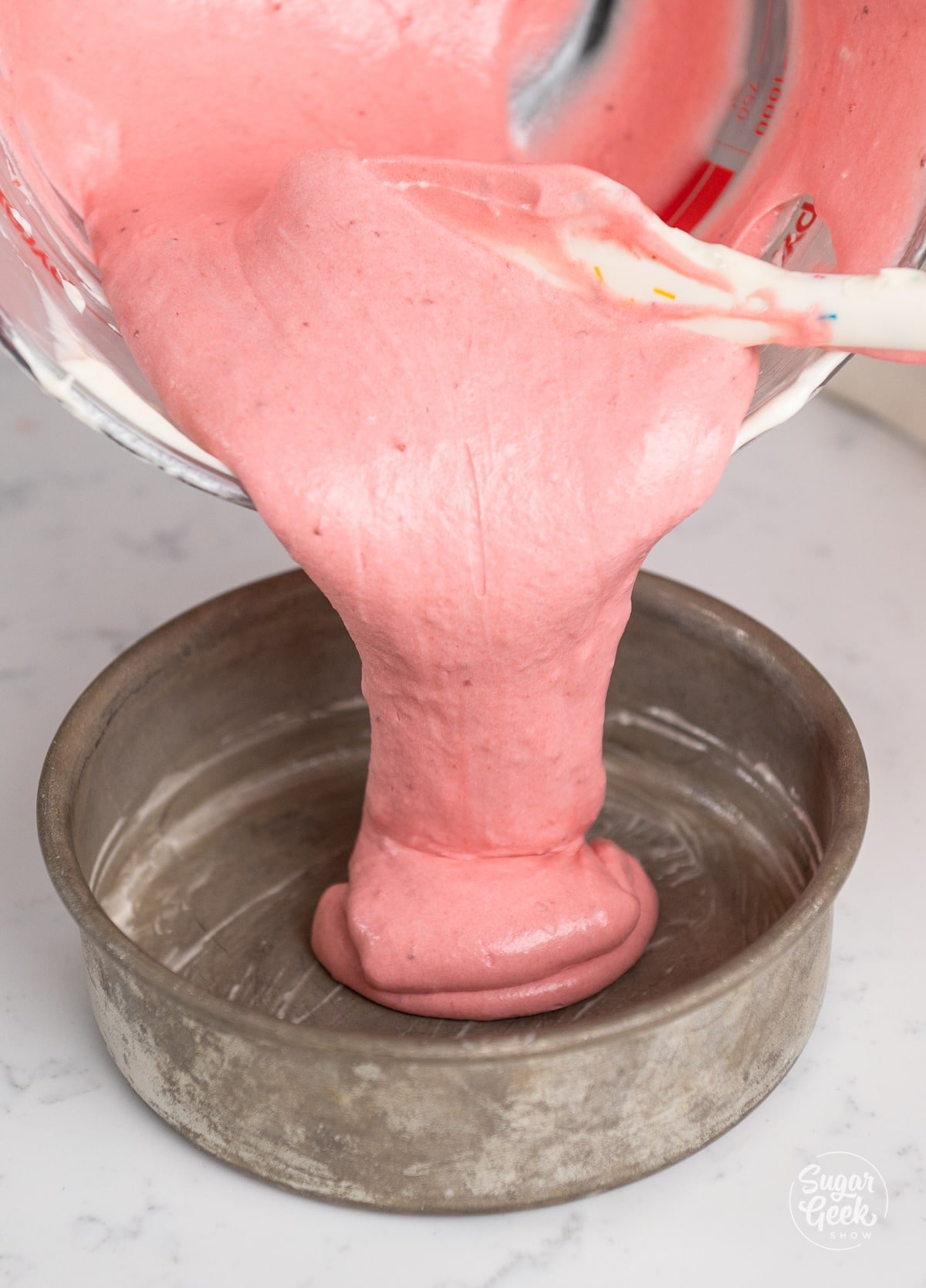 pouring strawberry cake batter into prepared pan. 