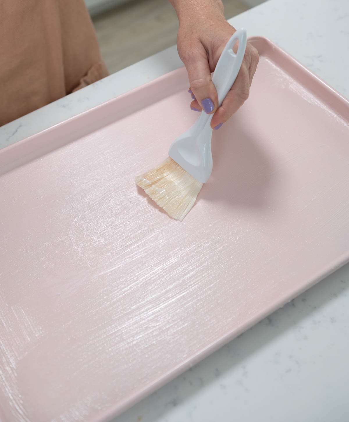 brushing cake goop on a pink sheet pan