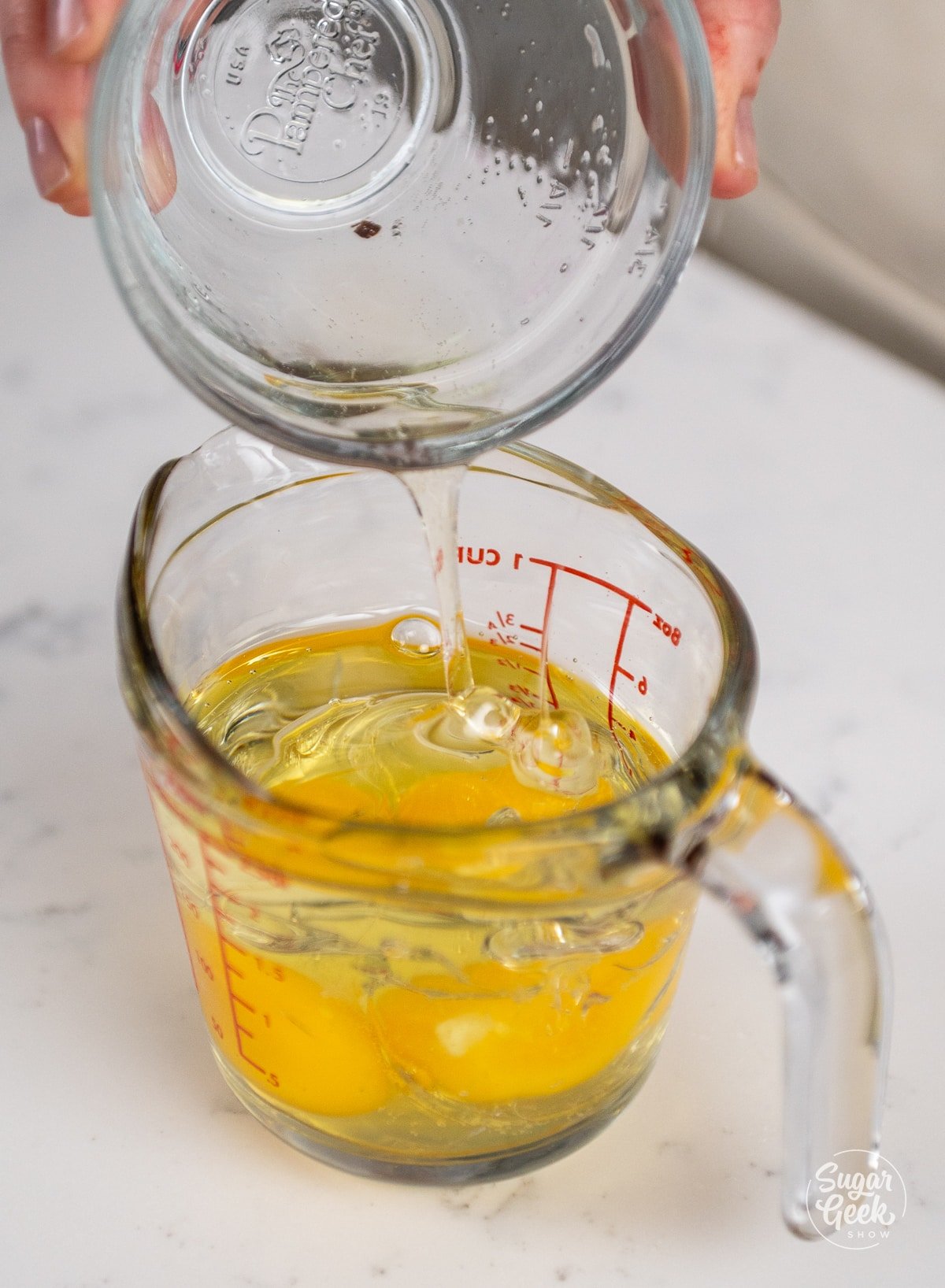 hand adding eggs to oil in a measuring cup.