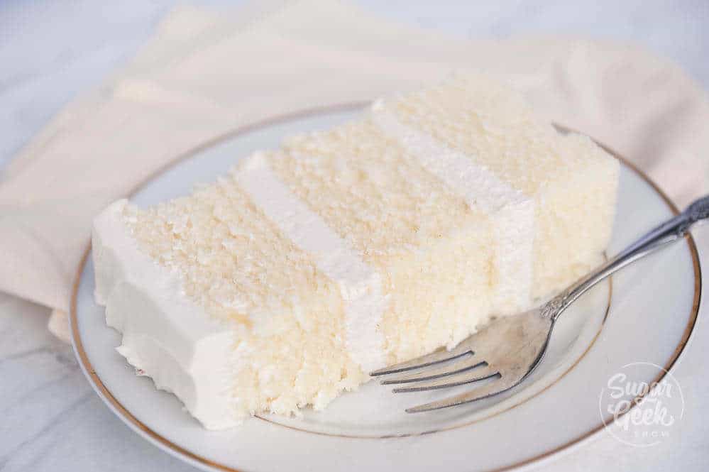 slice of white velvet cake with ermine frosting on a plate with a silver fork