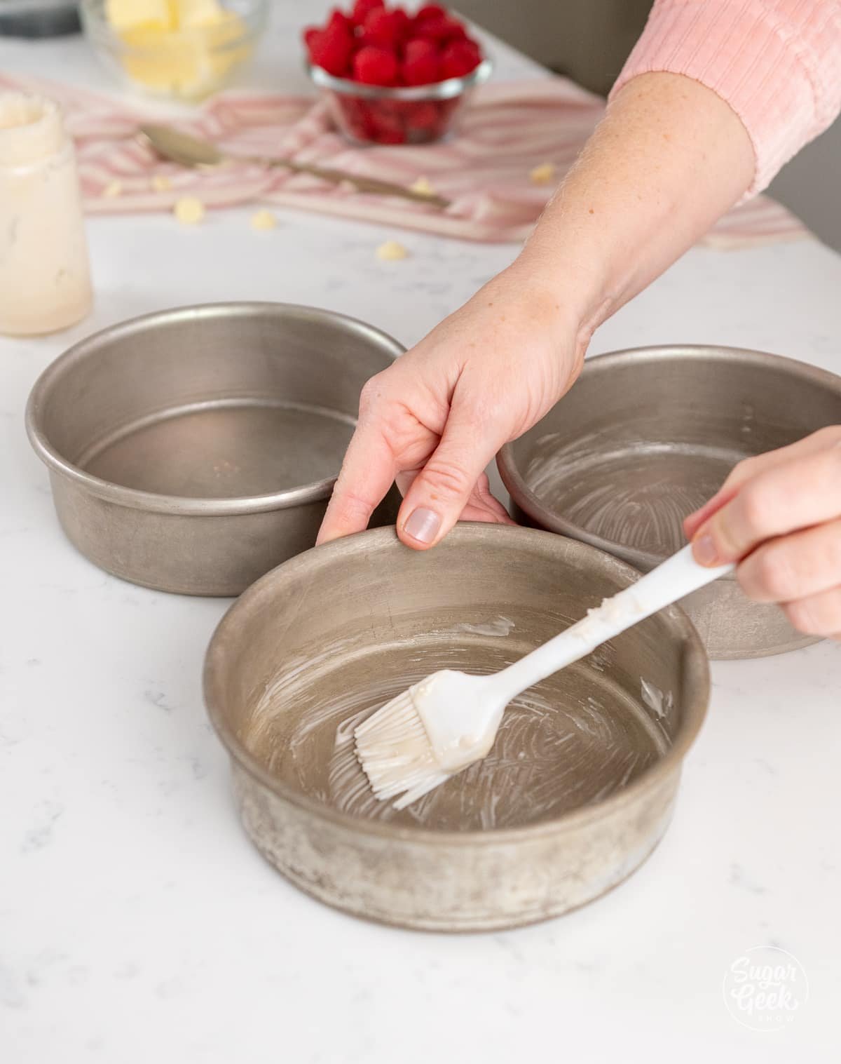 hands brushing cake release onto cake pans