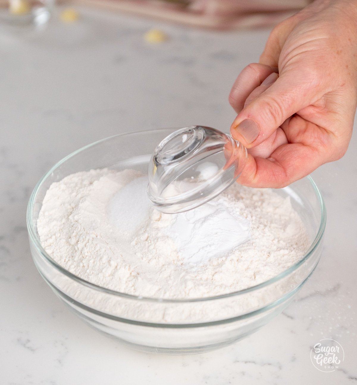 hand adding a small bowl of powder into a large bowl of flour