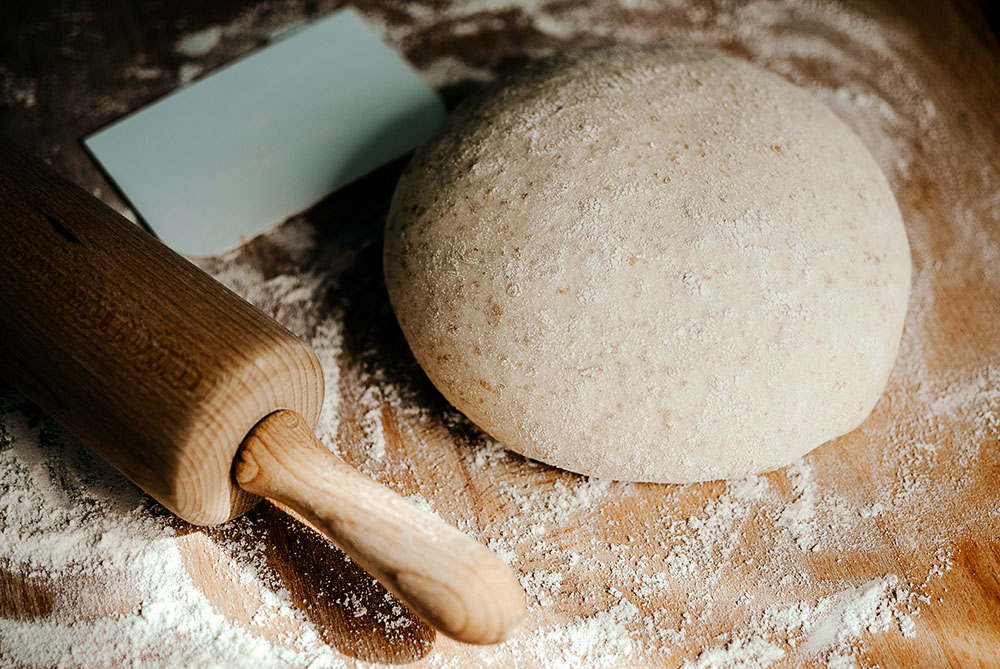 whole wheat bread dough on floured wooden surface with rolling pin